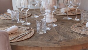 Una mesa de comedor dispuesta con copas de vino, platos y cubiertos, con un jarrón decorativo en el centro.