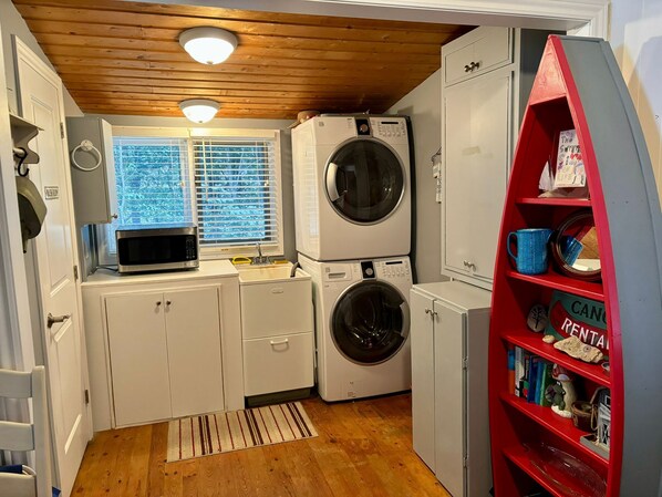 A compact laundry room with a washing machine, dryer, microwave, and a red storage unit with shelves.