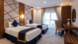 A hotel room with two beds, a desk, a chair, and a large window with curtains. - Al Qasr Hotel Suites - Al Wadiin (Ahad Rafidah)