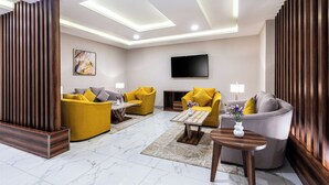 A modern living room with two yellow sofas, a grey sofa, a wooden coffee table, and a flat-screen TV mounted on the wall. - Al Qasr Hotel Suites - Al Wadiin (Ahad Rafidah)