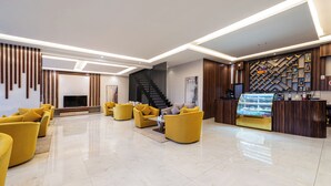 A modern lobby with yellow sofas, a fireplace, a staircase, and a reception desk with a display case. - Al Qasr Hotel Suites - Al Wadiin (Ahad Rafidah)