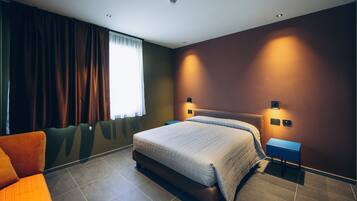A modern hotel room with a large bed, a small desk, and a seating area.