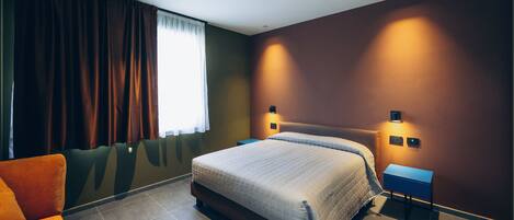 A modern hotel room with a large bed, a small desk, and a seating area.
