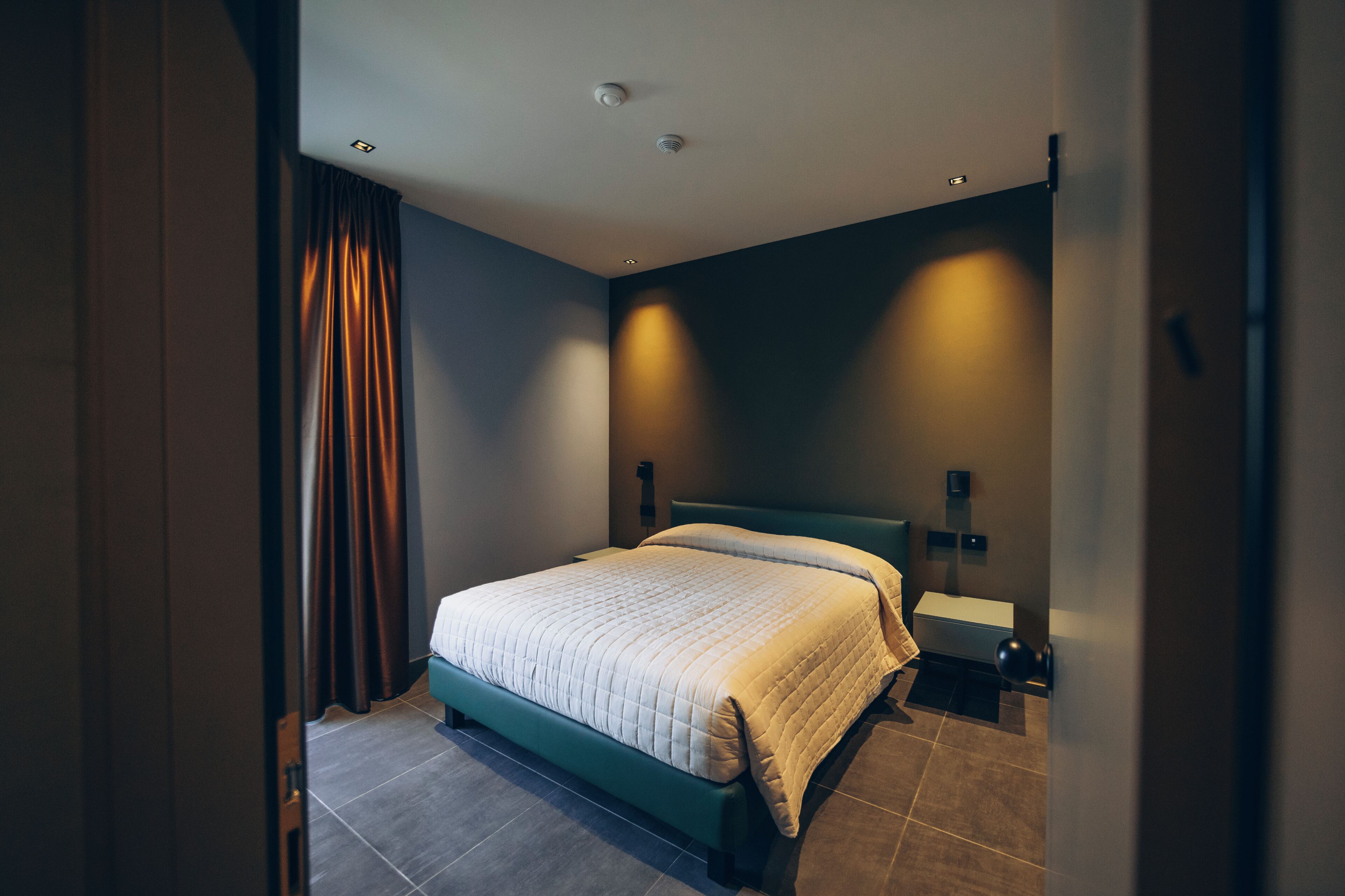 Una camera d'albergo moderna con un letto rifatto, un comodino e un punto luce a parete.