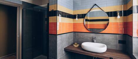 A modern bathroom with a glass shower enclosure, a white sink, and a mirror with a geometric frame.
