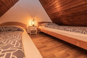 Acogedor dormitorio en ático con dos camas, paredes de madera y una mesita de noche con lámpara.