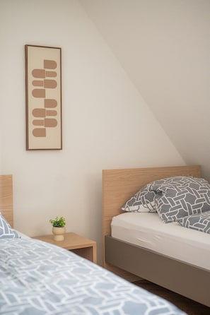 A bedroom with a bed, a bedside table with a plant, and a wall-mounted artwork.