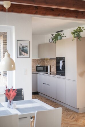 A modern kitchen with white cabinets, a microwave, and a stove. There is a bicycle hanging on the wall and a plant on the counter.