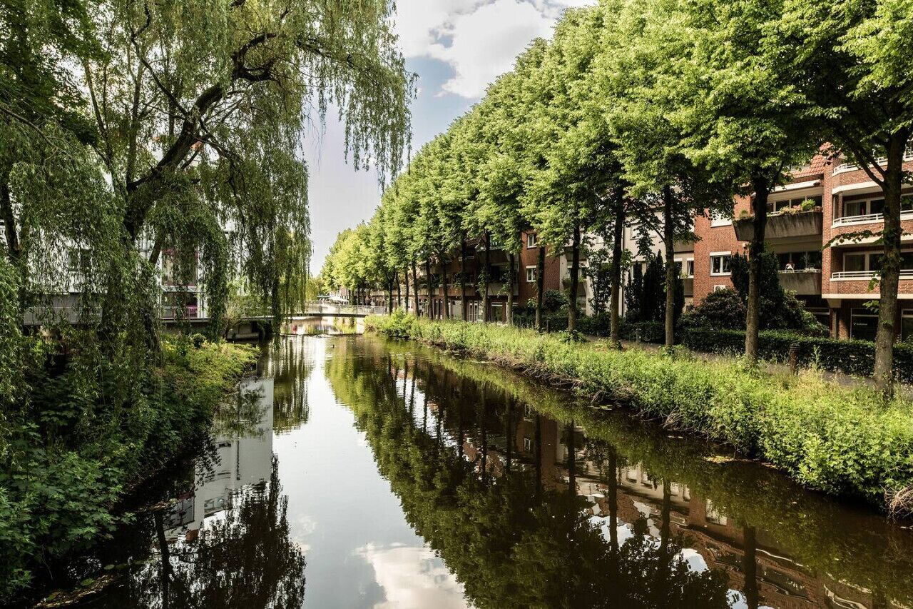 Un canal bordé d’arbres des deux côtés, un pont à l’horizon et des bâtiments dotés de balcons.