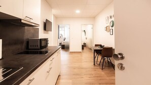 A modern kitchen with a microwave, a stove, and a dining area with a table and chairs. - FAIR BED 9 City Studio with kitchen, WLAN, 2 rooms & PP (Nordhorn)
