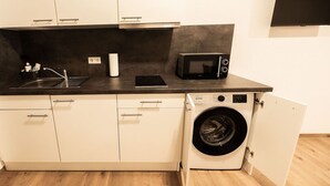 A compact kitchen with a washing machine, a microwave, and a sink. - FAIR BED 9 City Studio with kitchen, WLAN, 2 rooms & PP (Nordhorn)
