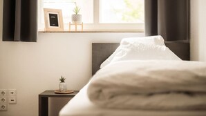 A neatly made bed with a white comforter, a small bedside table with a plant, and a picture frame on the wall. - FAIR BED 9 City Studio with kitchen, WLAN, 2 rooms & PP (Nordhorn)