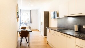 A modern kitchen with a dark countertop, light-colored cabinets, and a flat-screen TV mounted above the sink. - FAIR BED 8 City Studio with kitchen, bathroom, WLAN, & PP (Nordhorn)
