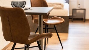 A modern hotel room with a wooden floor, a bed with white bedding, a small table with a chair, and a window with curtains. - FAIR BED 8 City Studio with kitchen, bathroom, WLAN, & PP (Nordhorn)