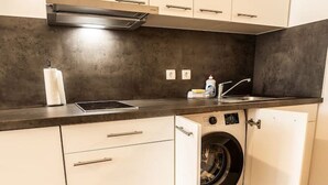 A compact kitchen with white cabinets, a built-in washing machine, and a dark countertop. - FAIR BED 8 City Studio with kitchen, bathroom, WLAN, & PP (Nordhorn)