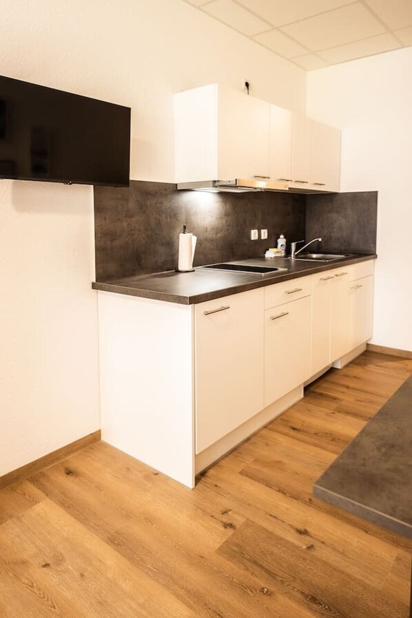 A modern kitchen with white cabinets, a black countertop, and a wooden floor.