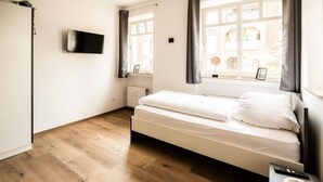 Camera da letto dal design minimalista con un letto, una TV a parete e una finestra con tende.
