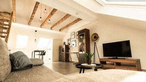 A spacious loft with exposed wooden beams, a large flat-screen TV, a cozy sofa, and a dining area with natural light. - Central studio - loft with WLAN & parking space (Nordhorn)