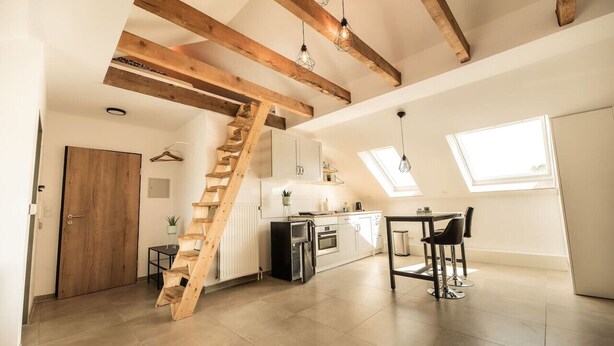 A spacious kitchen with a wooden staircase, a dining area with chairs, and a view of the outside through a skylight. - Central studio - loft with WLAN & parking space (Nordhorn)