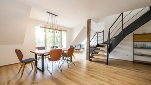 Una habitación amplia con piso de madera, una mesa de comedor con sillas, una escalera y un ventanal que proporciona luz natural.