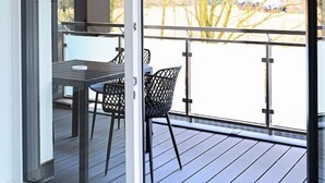 A modern balcony with a sliding glass door, a wooden deck, and a dining area with a table and chairs.