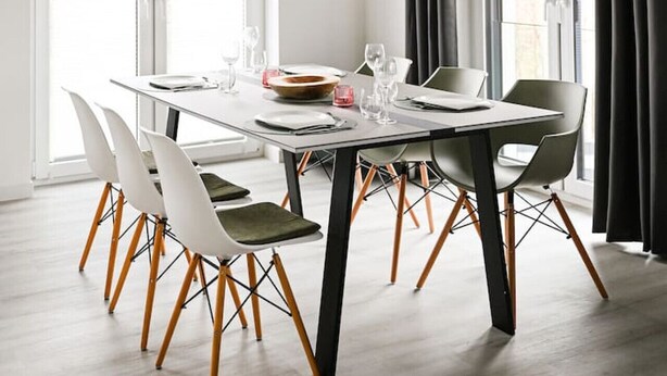 A modern dining area with a rectangular table, white chairs with wooden legs, and a unique chandelier.
