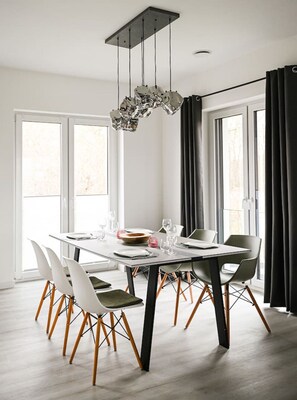 Un espace de salle à manger moderne, avec une table rectangulaire, des chaises blanches aux pieds en bois et un lustre original.