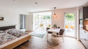 A modern bedroom with a bed, a desk, and a dining area. There is a sliding glass door leading to an outdoor patio. - "Vechte-Garten" new build with a view of the water & PP (Nordhorn)
