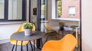 Une chambre moderne avec une porte vitrée donnant sur un balcon, une table ronde avec deux chaises et une plante en pot.