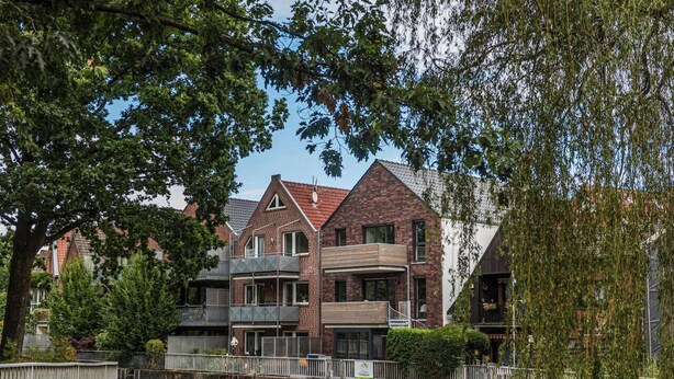 Un bâtiment situé au bord du canal, avec une façade en briques, de nombreux balcons et un petit pont enjambant l’eau.