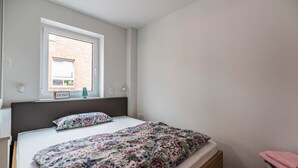 Une chambre à coucher avec un lit, une fenêtre, un panneau indiquant « MAISON », et une petite table avec une lampe.