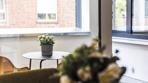 Une petite table ronde avec un pot de fleurs, placée sur un balcon doté d’un mur en briques et de fenêtres.