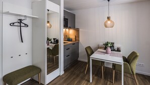 Une cuisine moderne avec un plan de travail en bois, un luminaire suspendu et un coin repas comprenant une table blanche et des chaises vertes.