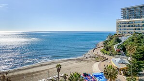 Un hotel frente a la playa con una carretera sinuosa que lleva a la costa, vista despejada del océano y un edificio con varios balcones que dan al mar.