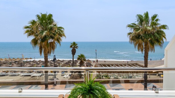 Un balcón con vistas a la playa, palmeras y al mar.