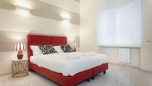 Une chambre d’hôtel moderne avec un lit rouge, du linge de lit blanc et deux lampes de chevet.