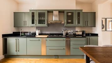 Une cuisine avec des meubles de couleur verte, une hotte de cuisinière en acier inoxydable et une table à manger en bois.