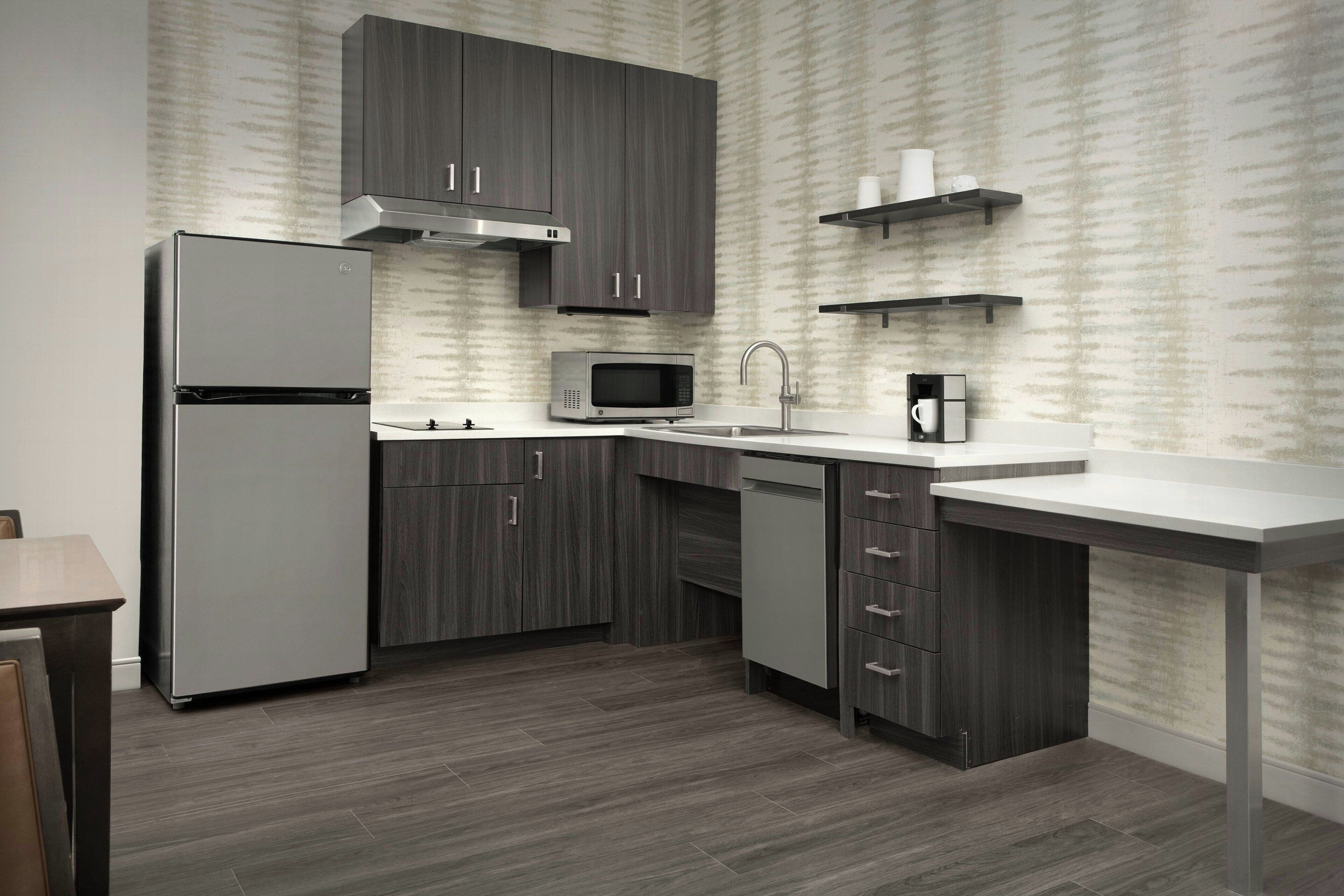 A modern kitchen with grey cabinetry, a stainless steel refrigerator, a microwave, and a coffee machine.