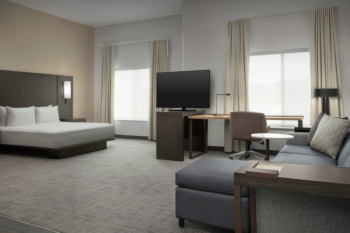 Quarto de hotel moderno com uma cama grande, uma mesa de escritório com TV de tela plana, um sofá confortável e uma pequena mesa.