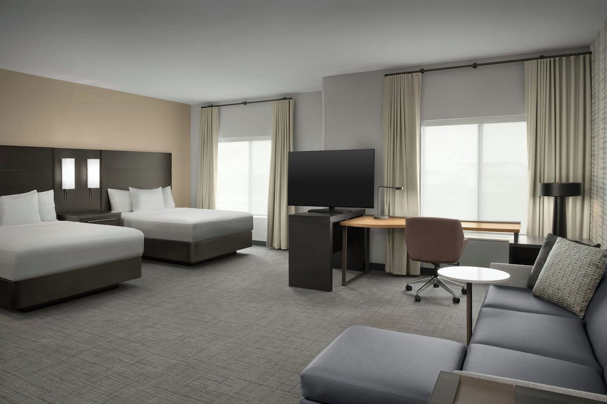 Quarto de hotel com cama, escrivaninha com televisão, sofá e cadeira.