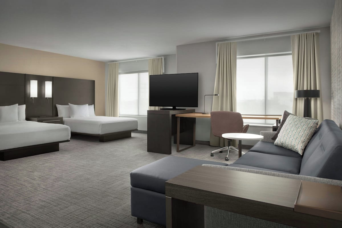 Quarto de hotel com uma cama grande, um sofá, uma televisão e uma escrivaninha.