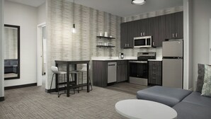Una cocina moderna con armarios de madera oscura, un refrigerador de acero inoxidable y un microondas. Hay un comedor con una mesa redonda y dos sillas.
