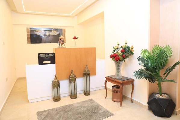 A reception area with a white desk, a framed poster, decorative lanterns, a vase with flowers, and a potted plant. - Pyramids Heart Hotel (Giza)