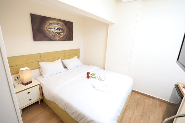 A neatly made bed with white linens, a bedside lamp, and a single red rose on the bed. - Pyramids Heart Hotel (Giza)