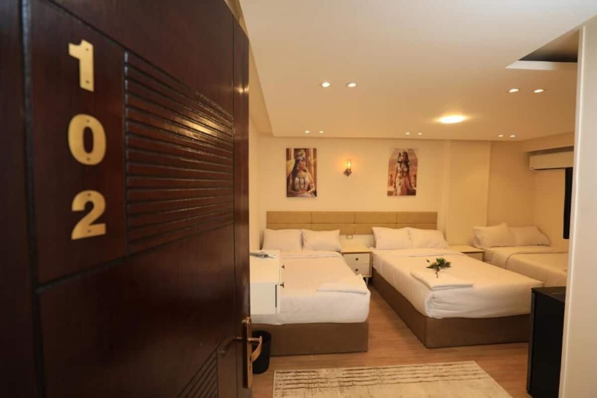 A hotel room with three beds, a wooden door with numbers, and a modern design.