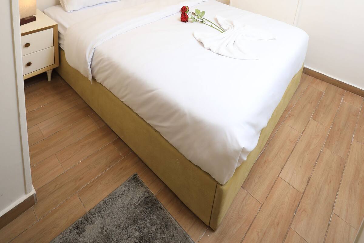 A neatly made bed with white linens, a headboard, and a single red rose on the bed.