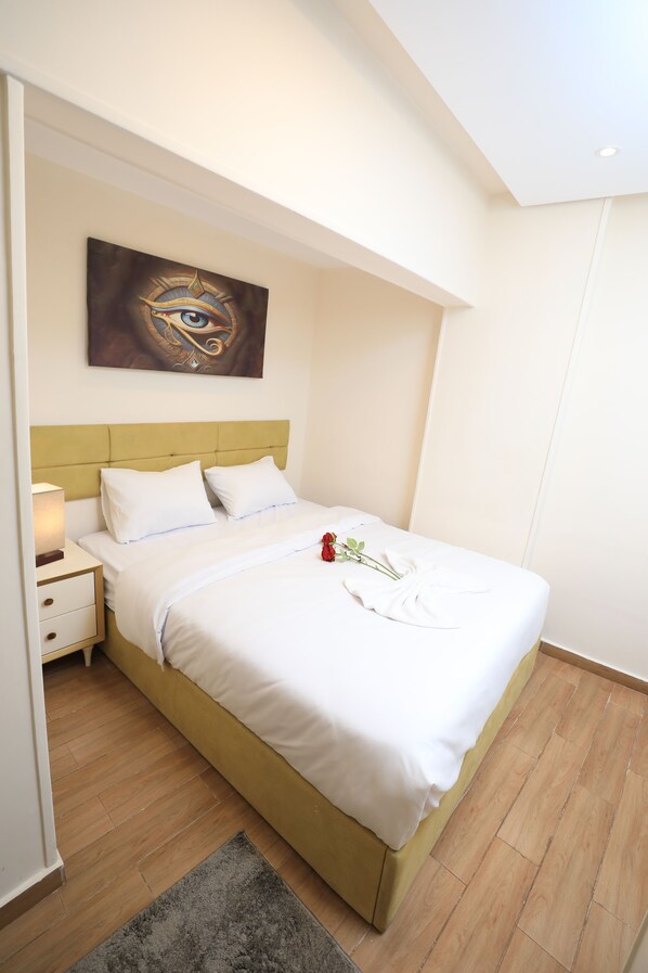 A neatly made bed with white linens, a headboard, and a single red rose on the bed. - Pyramids Heart Hotel (Giza)