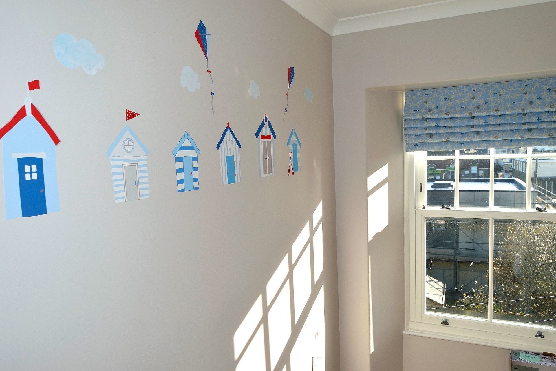 Une pièce avec une fenêtre et un mur décoré de découpages en papier représentant des maisons et des cerfs-volants.