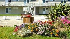 A residential building with a staircase leading to a balcony, surrounded by a well-maintained garden with various flowers. - Beach front apartment with direct beach access! (Perranporth)
