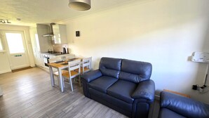 A compact living space with a kitchenette, a dining area, and a seating area with a sofa and chairs. - Beach front apartment with direct beach access! (Perranporth)